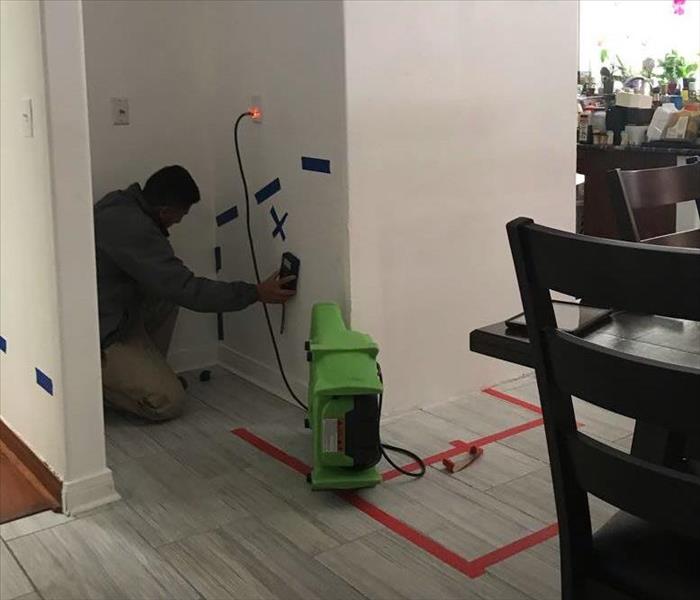 Drying equipment placed in kitchen with man using moisture meter on wall