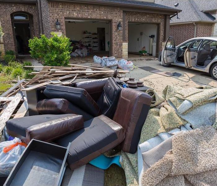 water damaged furniture, home items and ripped up carpet sitting on driveway of brick home