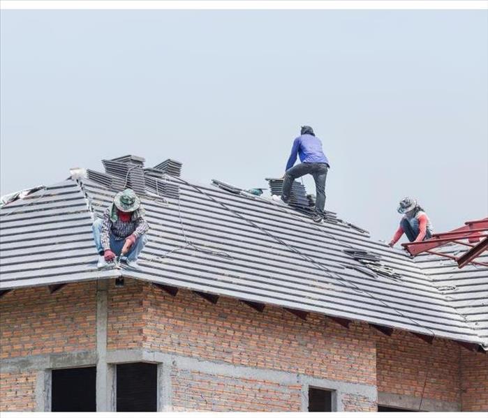 Workers installing concrete tiles on the roof while roofing house in construction site